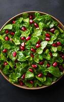 A bowl of salad with green spinach and red pomegranates. The salad is served in a brown bowl photo