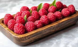 Raspberries artfully arranged in wood. Ripe raspberries are neatly arranged in a wooden tray, showcasing their vibrant color and inviting texture. photo