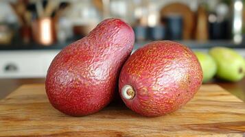 Bright red avocados rest on a wooden cutting board that highlights their unique color and texture, set against a stylish kitchen backdrop. photo