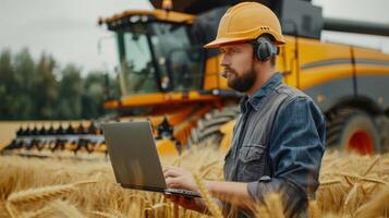 A farmer uses a laptop in a wheat field near a combine harvester. photo