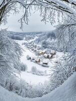 Aerial View of a Snow-Covered Village Surrounded by Frosty Trees and Rolling Hills in Winter Landscape Captured with a Circular Perspective photo