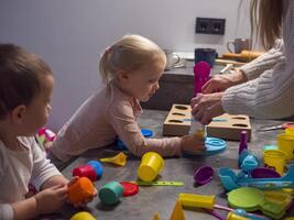 Mother and her two children are enjoying creative playtime together, shaping and molding vibrant plasticine dough into various forms on kitchen table, fostering imagination and family bonding photo