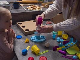 Mother and daughter create colorful ice cream using play doh toys in kitchen. Engaging with toys fosters creativity, bonding, and imaginative learning in warm and joyful home environment. photo