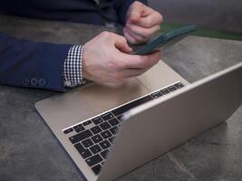 Businessman in blue suit and checkered shirt working at desk, using smartphone and laptop. Businessman focuses on tasks and communication Concept of remote work on computer Technology photo