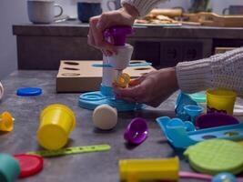 Woman enjoys play-doh ice cream set, crafting colorful creations on kitchen counter. Play-doh inspires fun and learning as she shares this engaging activity with family in lively atmosphere. photo