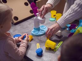 Mother and children enjoy creative playtime, shaping colorful modeling clay with tools and molds. Using tools enhances their creativity and brings fun to crafting vibrant shapes on the kitchen table. photo