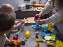 Mother and her two children enjoy creative playtime, building colorful ice cream tower using modeling clay and various tools. Vibrant modeling clay fosters imagination and fun in cozy kitchen setting photo
