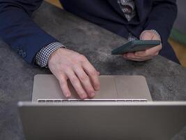 Businessman working remotely at modern office desk, managing tasks on laptop and holding smartphone. Businessman ensures effective communication and productivity Concept of remote work. photo