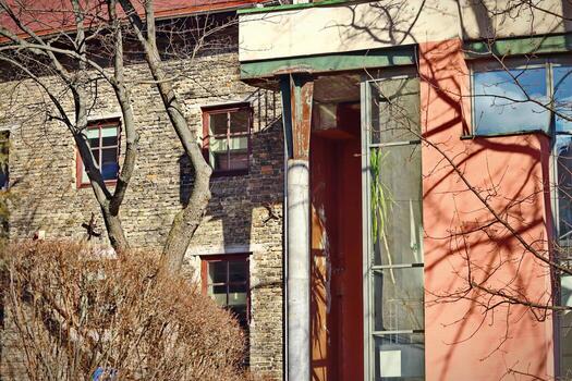 Old brown brick wall building behind leafless trees and a corner of a new red building with glass corner window with palm tree photo