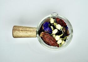 Organic earl grey tea, jasmine buds, lavender, gardenia, goji berry, and forget me not flowers in glass cup saucer container isolated on horizontal white background from above top view angle. photo