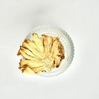 Dry sliced yellow pineapple fruits in round glass bowl isolated on square white background from above angle view. photo