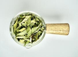 Group of dried green sliced pandan herb organic leaves in glass cup with wooden handle isolated on horizontal white background from top angle view. photo