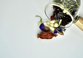 Group of spilled mixed organic earl grey tea, jasmine buds, lavender, gardenia, goji berry, and forget me not flowers in glass cup saucer container isolated on horizontal copy spaced white background. photo