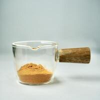 Turmeric powder in glass cup container with wooden handle isolated on square background. photo