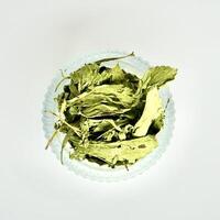 Crushed stevia plant leaves in round glass bowl isolated on square white background from above angle view. photo