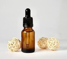 Brown transparent skin care bottle container with pipette cap with three rattan ball decoration isolated on horizontal white background. photo
