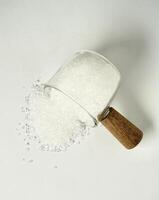 Pile of salt food flavoring ingredient spilled from glassware cup with wooden handle isolated on vertical white background from above angle view. photo
