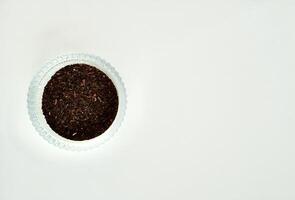 Pile of fragrant earl grey organic tea leaves in round glass bowl isolated on horizontal copy spaced white background from above angle view. photo