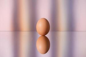 A single egg stands upright, reflected on a surface against pastel hues photo