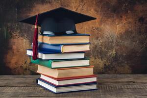 Stack of colorful books topped with a black graduation cap against rustic background photo