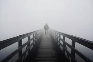 Solitary figure stands at the end of a narrow wooden bridge in thick fog photo