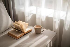 Serene room with a cozy couch, open book, and warm sunlight filtering through curtains photo
