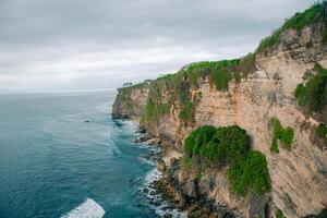 Overview panorama ocean shore, cliff. Sunset. Bali. Overwhelmed scene the flower and green-capped vertical cliff over the Indian ocean photo