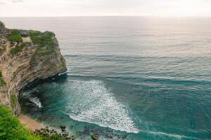 Overview panorama ocean shore, cliff. Sunset. Bali. Overwhelmed scene the flower and green-capped vertical cliff over the Indian ocean photo