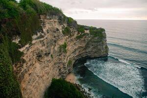 Overview panorama ocean shore, cliff. Sunset. Bali. Overwhelmed scene the flower and green-capped vertical cliff over the Indian ocean photo