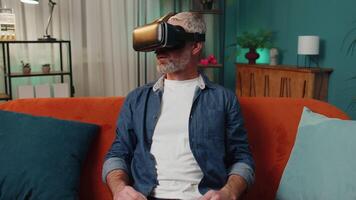 Old man using virtual reality futuristic technology headset to play simulation 3D game at home video