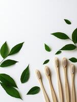 Eco friendly bamboo toothbrushes and green leaves on white background for sustainable living concept photo