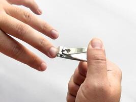 Close up of hands trimming fingernails with nail clipper on white background photo