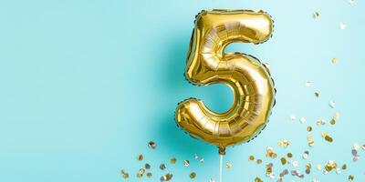 Helium filled golden number 5 balloon floating against teal background photo
