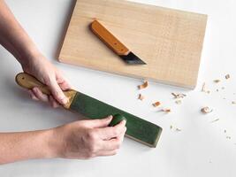 Hands sharpening tool with strop next to cutting board and carving knife photo