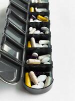 Weekly pill organizer with colorful capsules and tablets against a light background photo