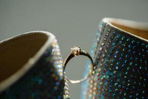Gold ring of the bride with a pebble between white shoes with heels. Bride's precious ring photo