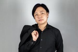 The portrait of a young Asian man wearing the tidy black suit with plain expression on the white grey background shot in the studio. photo