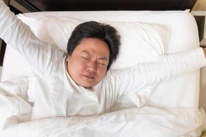 An Asian man begins his day with a refreshing stretch on the bed, feeling rejuvenated and content. photo