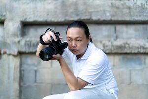 Professional Asian Chinese - Thai Camera man posture and focus in viewfinder and LED screen on mirrorless camera medium format in construction concrete area. photo