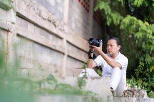 Professional Asian Chinese - Thai Camera man posture and focus in viewfinder and LED screen on mirrorless camera medium format in construction concrete area. photo