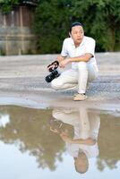 Asian man holds a big black mirrorless camera medium format type on cement asphalt ground in front of water reflex. photo