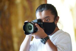 A man wearing black mask is shooting photo through a viewfinder camera with the right eye.