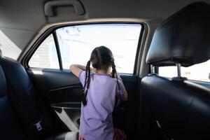 Backside of Little Asian 5 years old girl, is looking to the outside through car window mirror in the afternoon time. photo