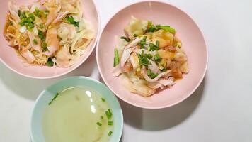 Two bowls of shrimp wonton noodles and a bowl of soup were placed on the table. photo