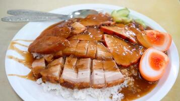 a plate of roasted red pork, crispy pork, and a perfectly half-boiled egg served atop a bed of steaming white rice, combined with the crunch of the crispy pork and the rich yolk photo