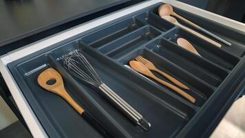 Different utensils in open desk drawer indoors, close up. Kitchen utensil such as spoon, ladle, scoop, handshake stored in box. photo