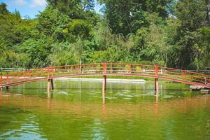 A model red bridge in a Japanese garden. Beautiful view of a model red bridge in a Japanese garden bridge reflects in water. photo
