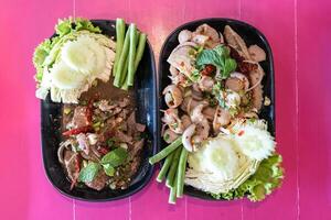 Larb Moo or Thai spicy minced pork salad with entrails and Larb Tub Wan or Thai spicy pork liver salad, a local Isan food in the northeastern part of Thailand, placed on the pink background. photo
