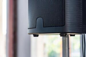The close up photo of the modern black speaker and the metallic stand on a blurry background.