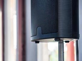 The close up photo of the modern black speaker and the metallic stand on a blurry background.